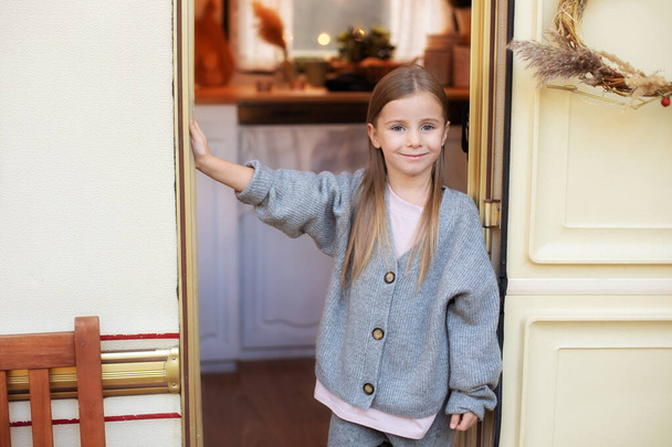 Portrait beautiful happy young girl with long hair. Smiling little girl in casual clothes standing on porch RV house in garden. Cute small girl stand near trailer door. Concept camping, adventure  - Photo, image