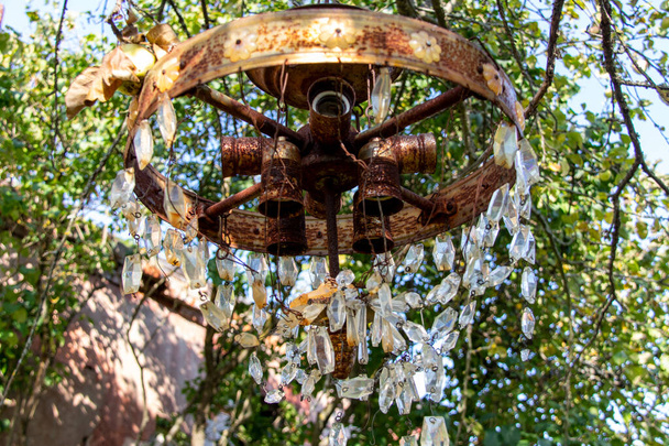 una vieja araña oxidada con colgantes de vidrio cuelga de una rama de árbol - Foto, Imagen