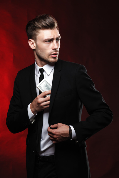 Handsome young man in suit on dark background with money - Valokuva, kuva