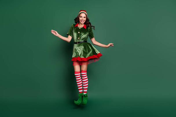 Full length photo of young girl elf happy positive smile jump up christmas time holiday isolated over green color background - Fotó, kép