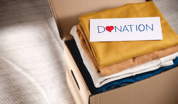 Концепція донорства одягу. Коробка тканини з етикеткою пожертвування. Приготування старого одягу вдома. Вид зверху
 - Фото, зображення