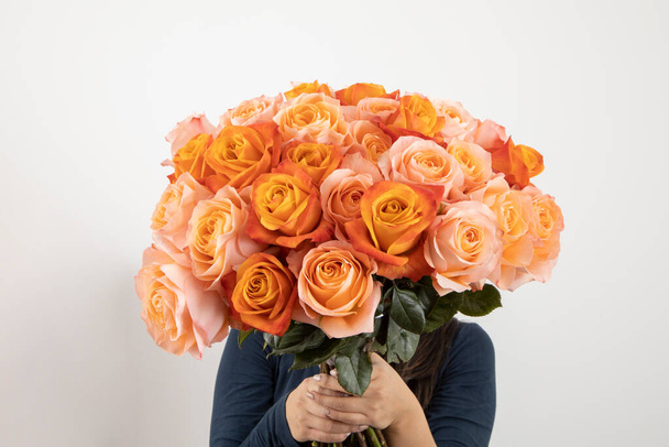 personne tenant et cachant son visage avec un grand bouquet de roses colorées, cadeau romantique de Saint-Valentin, en studio, style de vie et nature - Photo, image