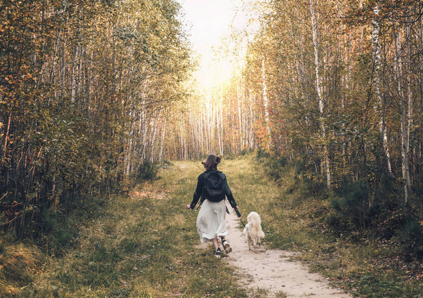 back view of young woman running with her dog along a path in the forest. walking with pets, togetherness concept. - Photo, Image