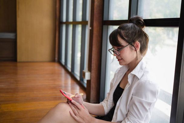 Νεαρή γυναίκα με πιτζάμες που χρησιμοποιεί έξυπνο τηλέφωνο στο σαλόνι. - Φωτογραφία, εικόνα