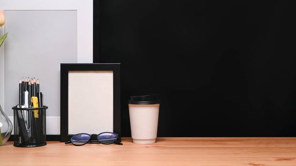 Marco de imagen vacío, portalápices, vasos y taza de café en la mesa de madera. - Foto, Imagen