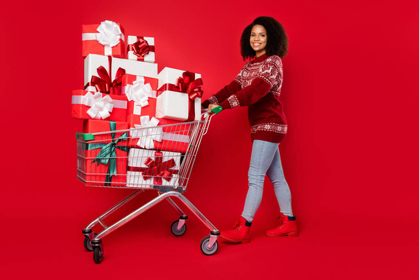 Fénykép csinos bájos nő öltözött nyomtatott pulcsi mosolygós vásárlás ajándékok elszigetelt piros szín háttér - Fotó, kép
