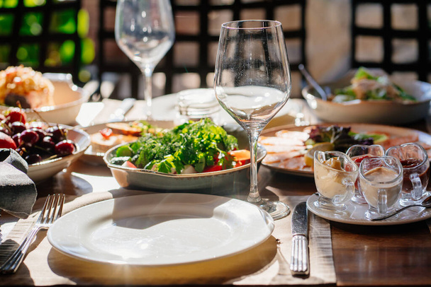 mesa de madera servida con platos con ensalada y aperitivos en la terraza abierta - Foto, imagen