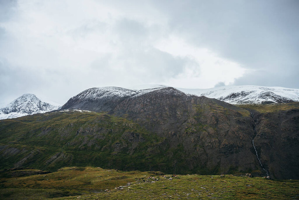 Минималистский альпийский пейзаж со снежными горами в низких облаках в пасмурную погоду. Глубокое ущелье на фоне заснеженной горной цепи под низким облачным небом. Атмосферный минимализм в высоких горах. - Фото, изображение