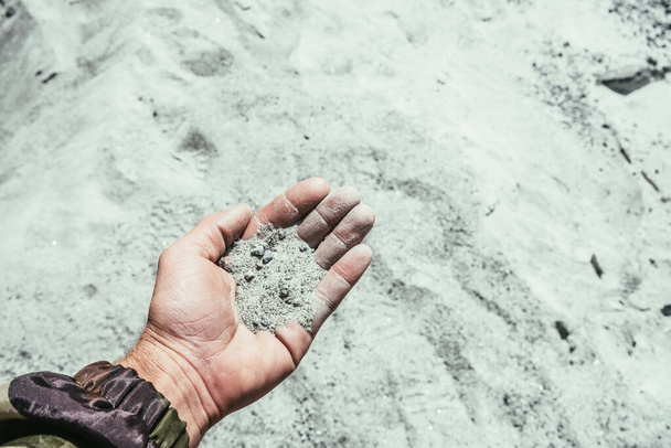 De mens houdt handvol glimmend zand in de hand op een wazige zandachtergrond. Menselijke palm met handvol prachtig wit grijs zand met kleine steentjes in zonlicht. Mens met kleine kristallen en mineralen in de hand. - Foto, afbeelding