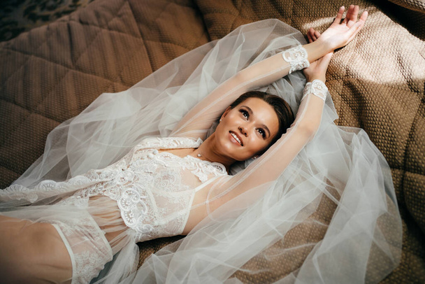 krásná nevěsta v krajkovém županu leží v posteli na závoji. ráno před svatbou - Fotografie, Obrázek