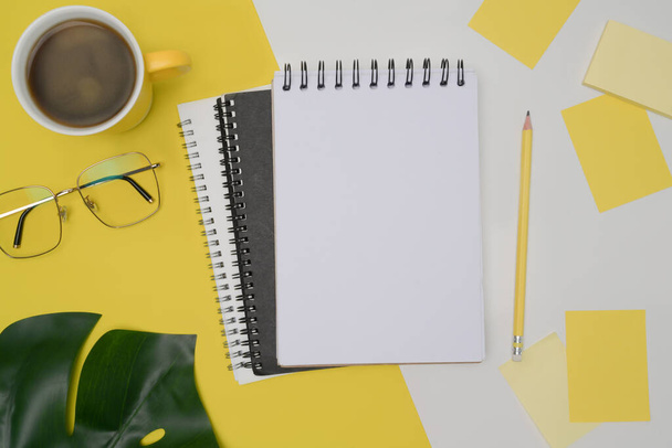 Draufsicht leeres Notizbuch, Gläser, Kaffeetasse und Haftnotizen auf gelbem Hintergrund. - Foto, Bild