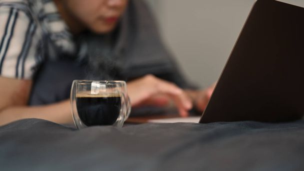Egy csésze kávé az ágyon egy férfival, aki laptopot használ reggel.. - Fotó, kép