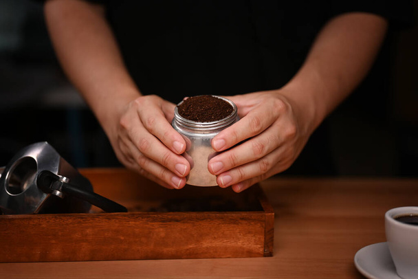 Barista holding moka pot with  ground coffee in dark room. - Zdjęcie, obraz