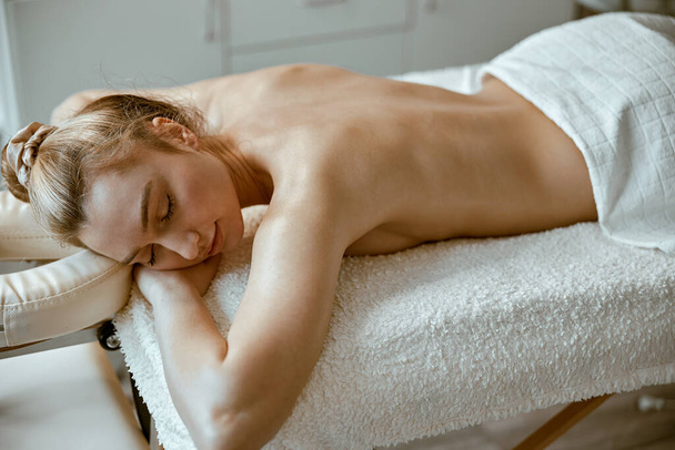 beautiful slim caucasian woman is relaxing on therapist table in spa salon - Photo, Image