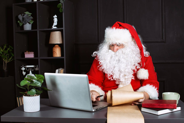Święty Mikołaj pracuje w biurze dla laptopa. - Zdjęcie, obraz