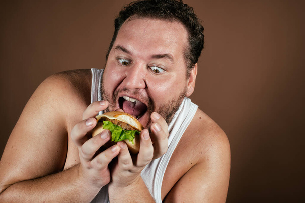 Dieta e stile di vita sano. Uomo grasso divertente con un hamburger. - Foto, immagini