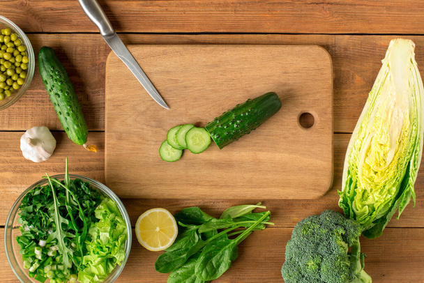 Verse groenten voor salade liggen op een houten tafel met een snijplank. Bovenaanzicht. - Foto, afbeelding