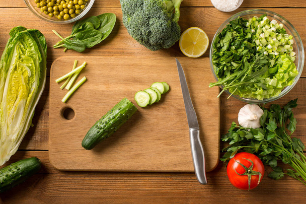 Las verduras frescas para la ensalada se acuestan sobre la mesa de madera con la tabla de cortar. Vista superior. - Foto, Imagen