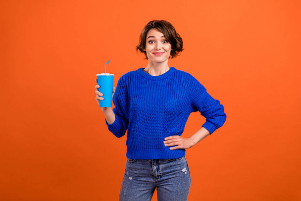 Photo of cute brunette young lady hold cup wear blue pullover isolated on orange color background - Фото, изображение