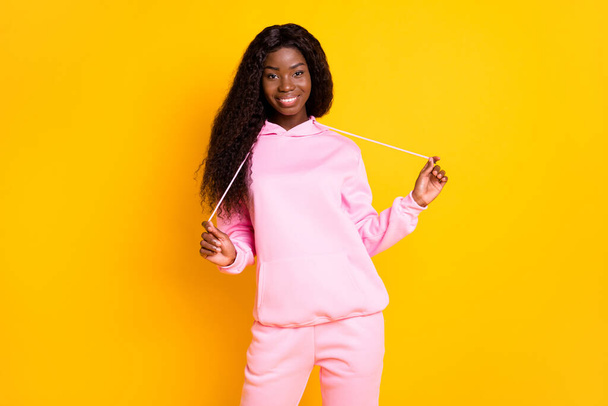 Photo portrait of african american girl pulling hoodie strings laces isolated on vivid yellow colored background - 写真・画像