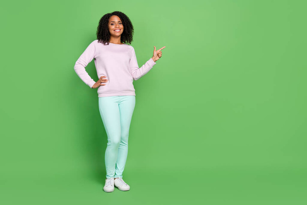 Full length photo of nice millennial brunette lady point empty space wear sweater pants sneakers isolated on blue background - 写真・画像