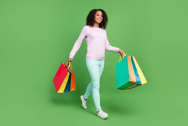 Full length photo of good millennial brunette lady hold bags go wear sweater pants sneakers isolated on blue background - Foto, afbeelding