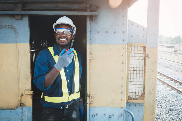 Αφρικανός μηχανικός φοράει γυαλιά ασφαλείας, κράνη και γάντια για την πρόληψη ατυχημάτων κατά την εργασία με την ομιλία με ραδιοεπικοινωνία ή walkie talkie - Φωτογραφία, εικόνα