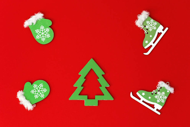 New Year flat lay from homemade wooden toys, small green mittens and skates, christmas tree on red paper background. Holiday concepts. - Фото, зображення