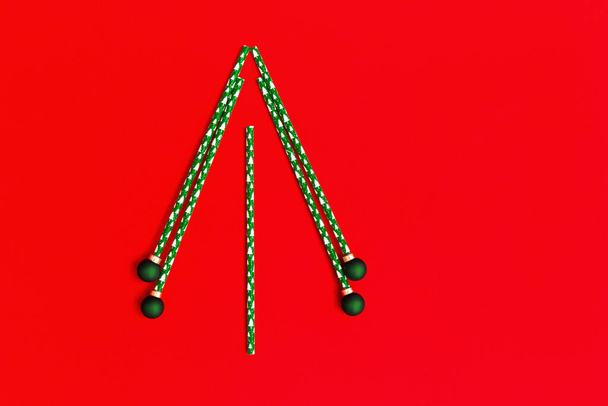 Creative christmas tree from drinking straws and green New Year balls on red background. Holiday winter concept with bright colors. Minimal flat lay. - Фото, изображение