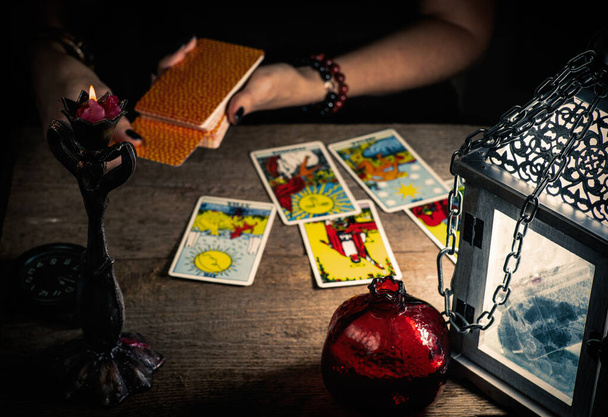 Ο μάντης απλώνει σε ένα ξύλινο τραπέζι τις κάρτες ταρώ με το φως ενός φαναριού και ενός κεριού. Επιλεκτική εστίαση. - Φωτογραφία, εικόνα