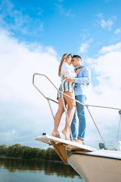 Young couple hugging on deck of sailboat. Romantic couple on a pleasure boat. Happy wealthy man and a woman by private boat have sea trip. Couple on honeymoon traveling with yacht - Фото, изображение