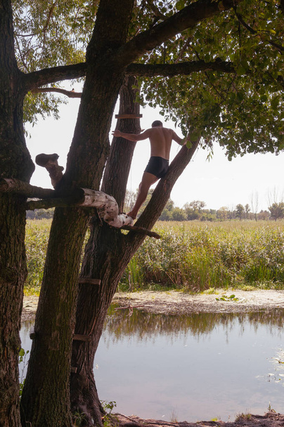 Een jongeman staat op een boom boven de rivier. Kwaliteitsbeeld voor uw project - Foto, afbeelding