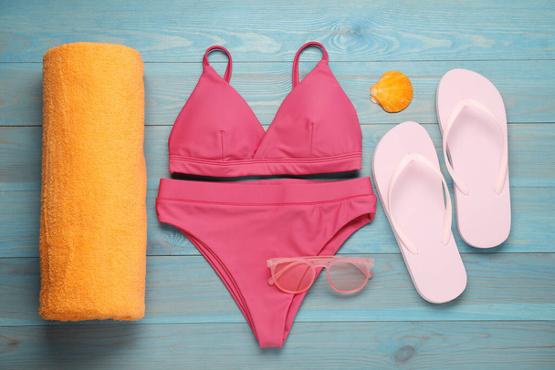 Beach towel, swimsuit, sunglasses and flip flops on light blue wooden background, flat lay - Foto, Bild