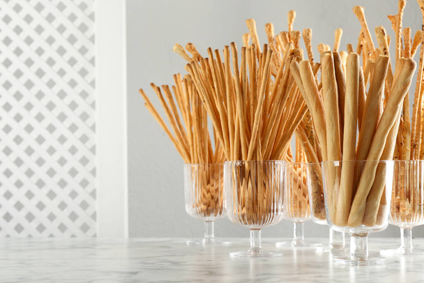Delicious grissini sticks served in glasses on white marble table. Space for text - Foto, Bild