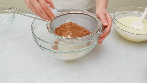 Suklaakakku askel askeleelta resepti. Kuivien ainesosien - jauhojen, kaakaojauheen, leivinjauheen - sekoittaminen lasikulhossa, lähikuva - Valokuva, kuva