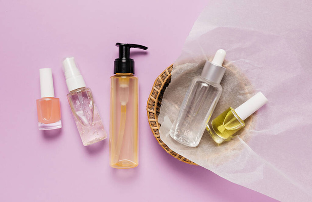 Organic cosmetics packaging design. Flat lay, top view clear glass pump bottle, brush jar, moisturizing serum jar in a paper basket on a purple background. Natural cosmetics SPA - Фото, зображення