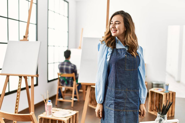 Young artist woman at art studio looking away to side with smile on face, natural expression. laughing confident.  - 写真・画像