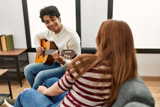 Junges Paar lächelt glücklich und spielt klassische Gitarre zu Hause auf dem Sofa. - Foto, Bild