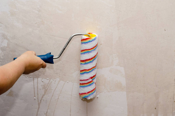 A woman holds a paint roller and impregnates the walls of the ro - Photo, Image