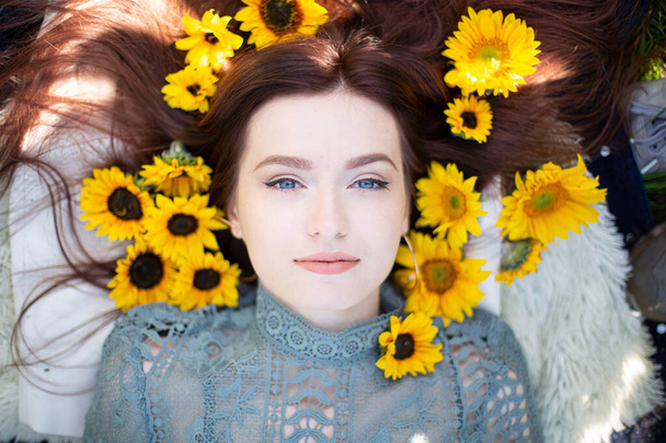 Young girl with dark hair and blue eyes lying portrait within sunflowers - Photo, Image