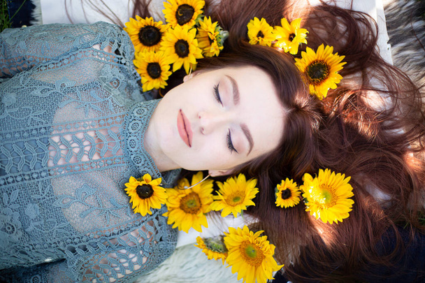 Young white girl with dark hair lying portrait with closed eyes within sunflowers - Valokuva, kuva