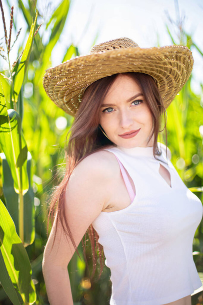 Smiling white young girl with dark hair in straw hat in the tall grass - Photo, Image
