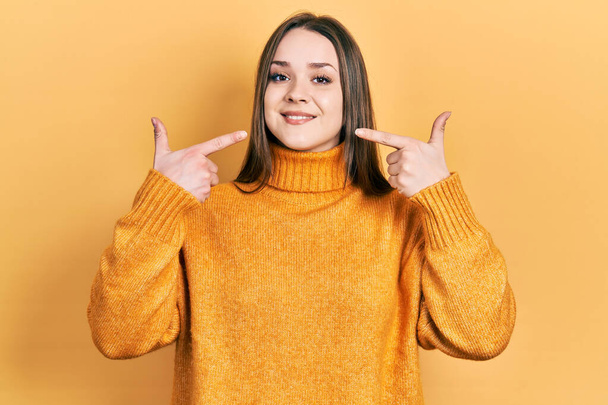 Young hispanic girl wearing casual clothes smiling cheerful showing and pointing with fingers teeth and mouth. dental health concept.  - Foto, Imagen