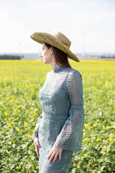 White girl with dark hair standing in yellow blooming field looking away - Valokuva, kuva