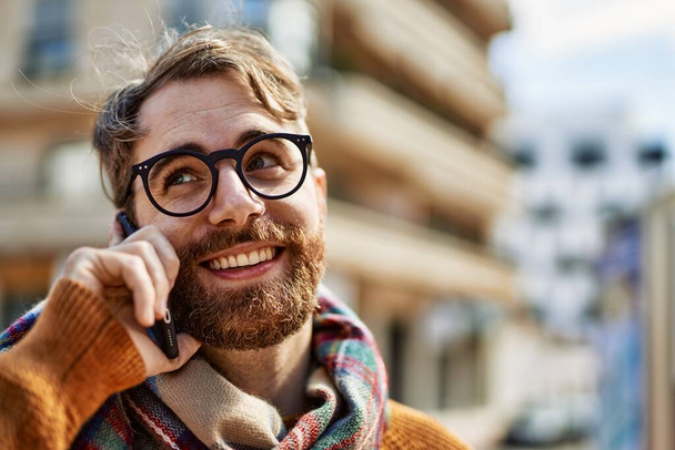 Caucasian man with beard having a conversation speaking on the phone outdoors on a sunny day - 写真・画像