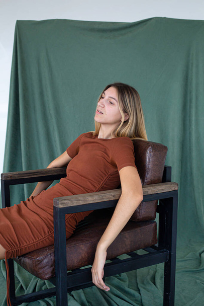 European girl sitting in a chair partially green background in studio - Zdjęcie, obraz