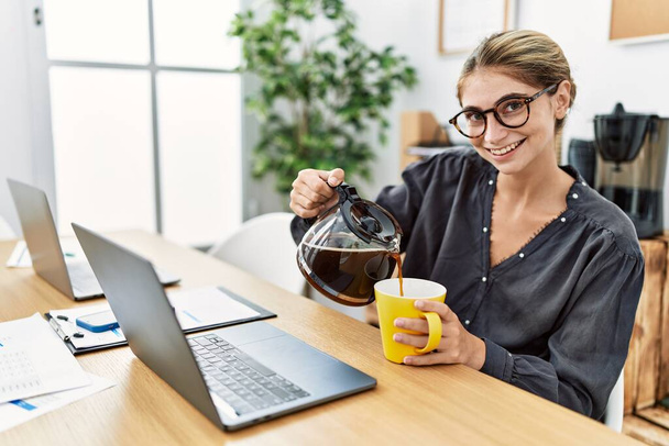 Joven mujer caucásica bebiendo café trabajando en la oficina - Foto, imagen