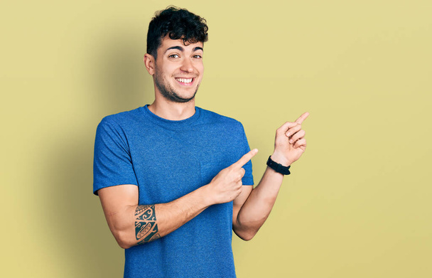 Joven hombre hispano vistiendo camiseta casual señalando a un lado preocupado y nervioso con ambas manos, preocupado y sorprendido expresión  - Foto, Imagen