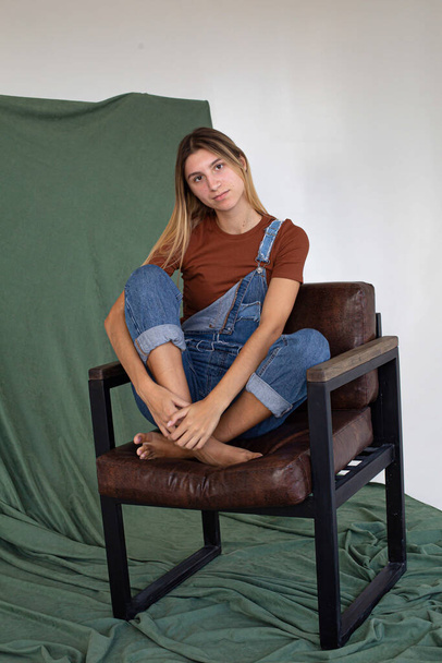 Pretty white woman sitting in a chair partially green background in studio - Фото, зображення