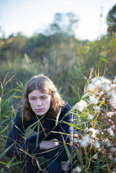 Smutny biały młodzieniec z długimi włosami na zielonej trawie - Zdjęcie, obraz